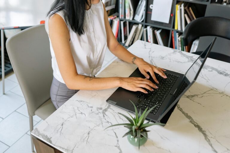 A professional woman typing on a laptop in an office environment, featuring a modern marble table.