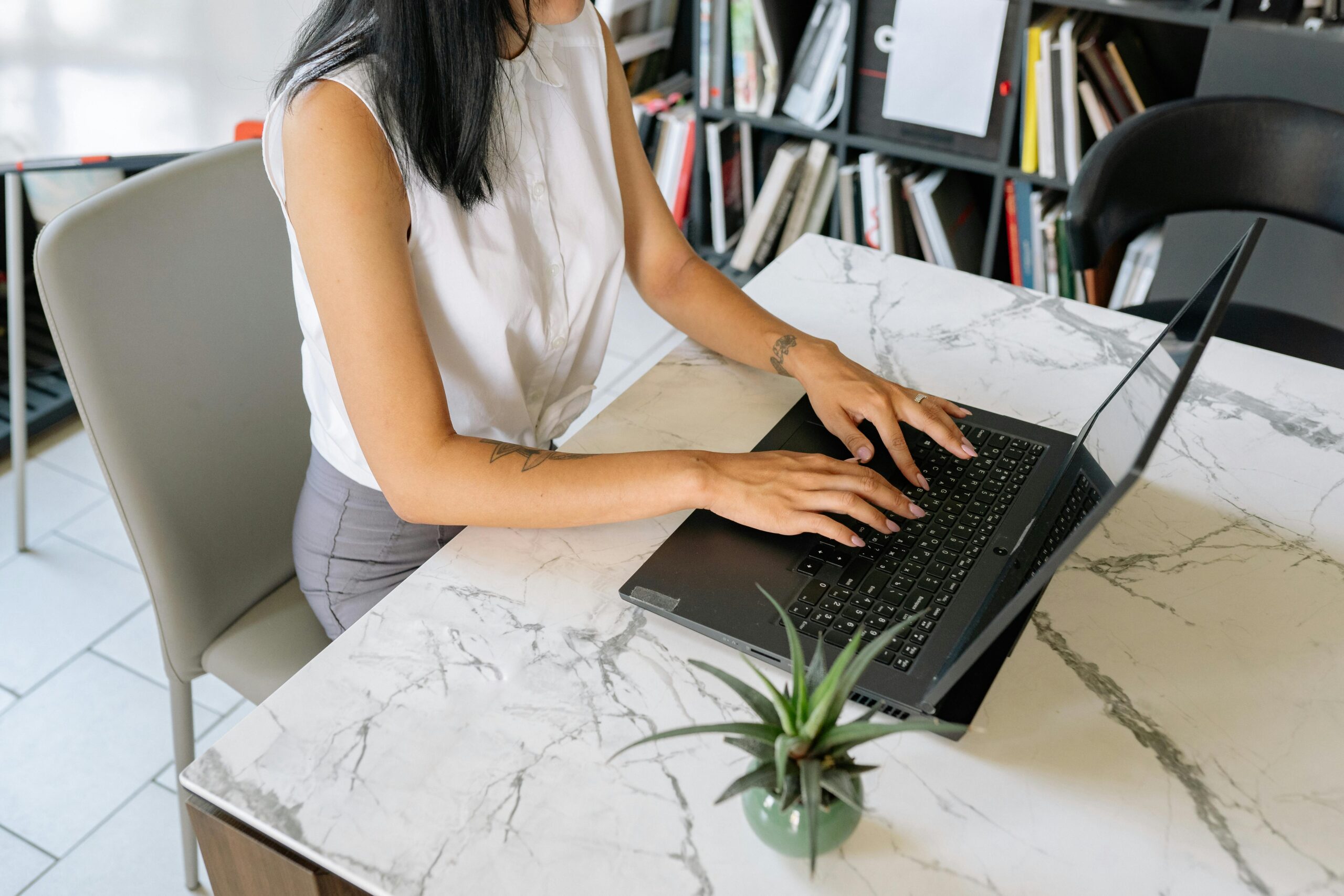 A professional woman typing on a laptop in an office environment, featuring a modern marble table.